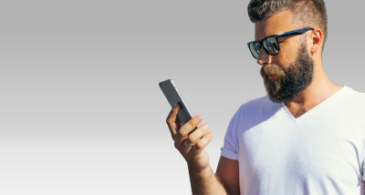 man with bear wearing sunglass readers reading his phone